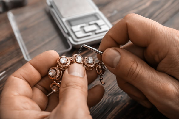 Jeweler fixing chain on wooden background, closeup