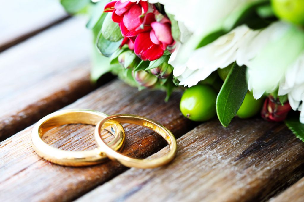 Goldene Trauringe vor Blumengesteck